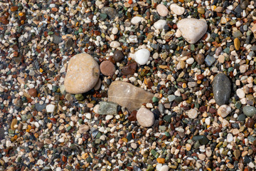 Thin white foam and the many small bubbles on the glittering sea water with the colorful pebbles underneath
