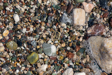 Thin white foam and the many small bubbles on the glittering sea water with the colorful pebbles underneath