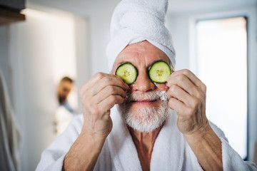 Senior man with cucumber on front of his eyes in bathroom indoors at home.
