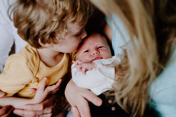 A small boy kissing a newborn baby brother at home.