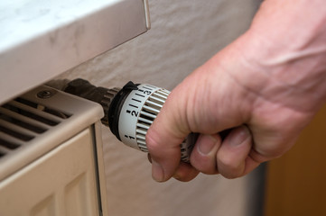 A man has a thermostat on a heater is set to a small level to save energy. Concept: heat or heating...