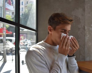 Fototapeta na wymiar A young man suffers symptoms of a cold, flu or allergy, and blows his nose in a tissue