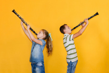 A boy and a girl with clarinets are standing with their backs to each other, playing the clarinet,...