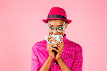 Portrait of a smart young woman with glasses drinking a coffee mug and looking to side, isolated on pink studio background.