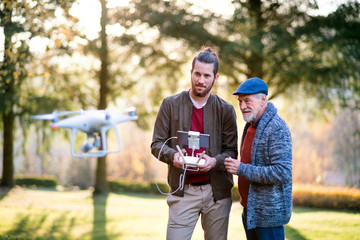 Senior father and his son with drone in nature, talking.