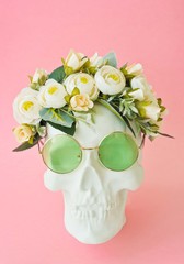 Human skull with green glasses and flowers on white background