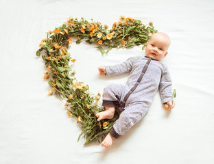 Smiling baby shapes heart with flowers on white background