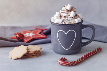 Mug of hot chocolate with whipped cream, marshmallows and red Lollipop, red star, cookies on a grey background. Hot winter drink