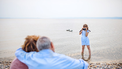 Small girl with camera and grandparents on holiday ba lake, taking photos.