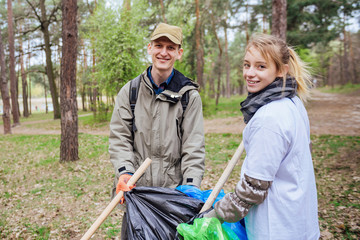 Man and woman are picking up the garbage and putting it in a black and blue garbage bags in a...