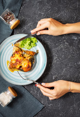 Female hands hold knife and fork. Baked eggplant with cheese on a stone table. Parmigiana melanzane.
