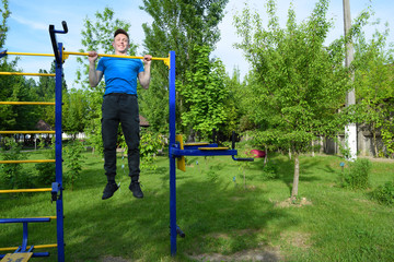 Fototapeta premium A young man pulls up on a horizontal bar in the city Park.