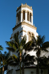 Fototapeta na wymiar The setting sun highlights one side of a white bell tower and palm trees - Our Lady of Sorrows Church in Santa Barbara, California