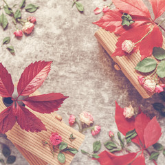 Red leaves are in a small vase on a wooden box. Nearby are scattered small dried roses. Autumn composition. Flat lay.