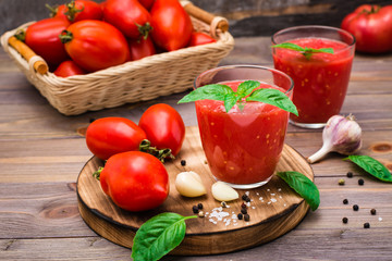 Fresh tomato juice with basil leaves in glasses and tomatoes on a wooden table