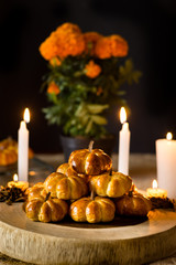 Pumpkin bread placed in a pyramid on a circular wooden base, traditional Mexican recipe, decorated with candles and cempasuchil flowers, diffuse background, commemorating the Day of the Dead.