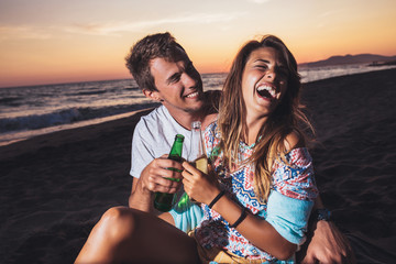 Young couple at the beach having fun, laughing and drinking beer