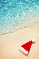 Christmas holidays concept. Top view of santa claus hat on summer sand beach.