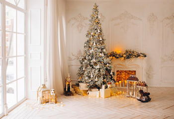classical interior of a white room with a decorated fireplace, luxury Christmas tree, garlands, candles, lanterns, gifts. day. pink sofa pastel colors