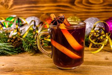 Cup of mulled wine with cinnamon, christmas decorations and fir tree branches on wooden table