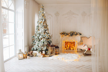 classical interior of a white room with a decorated fireplace, luxury Christmas tree, garlands, candles, lanterns, gifts. day. pink sofa pastel colors