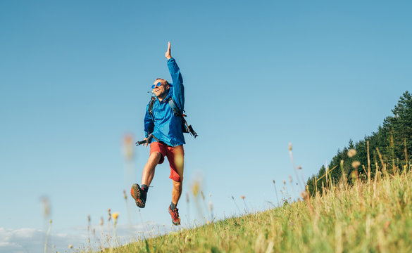 Backpacker traveler emotionally jumping over green grass mountain meadow with backpack with wide opened arms and legs. Human's freedom in nature concept image.