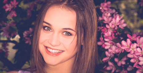 Portrait of young woman in the flowered garden in the spring time. Blossom background.