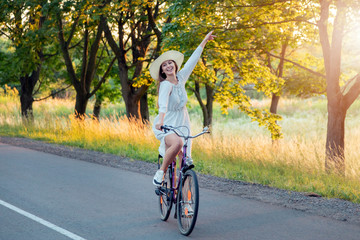 Fototapeta premium Cute cheerful girl in white dress playing fool while riding her bicycle