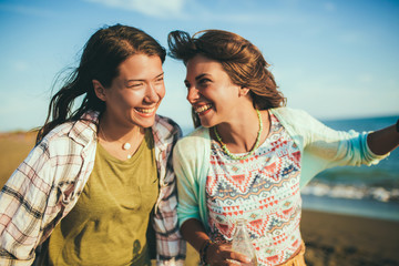 Portrait of two young female friends walking on the sea shore laughing.