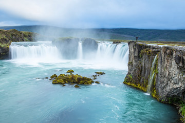 Godafoss, Iceland »; August 2017: A young girl at the top of the Godafoss waterfall with the impressive waterfall in the background