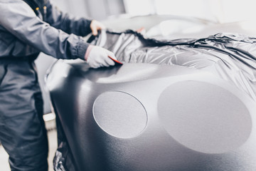 Car wrapping specialist putting vinyl foil or film on car. Selective focus.