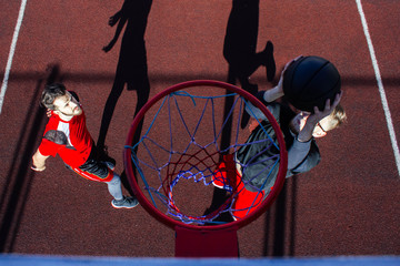 The moment of the shot on the basketball hoop. A ball is played between two basketball players. Young athletes on a sports basketball court in a jump make a dunk throw. Sport and active lifestyle. © Daniil