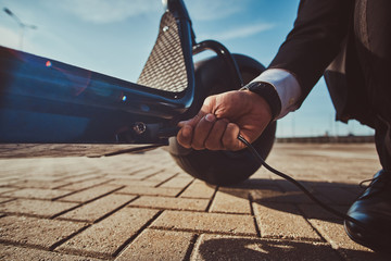 Elegant man is charging his electrical scooter with charger on special parking. © Fxquadro
