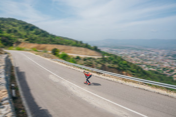 Male hipster wearing a hat and a red shirt is riding a longboard downhill on an open road