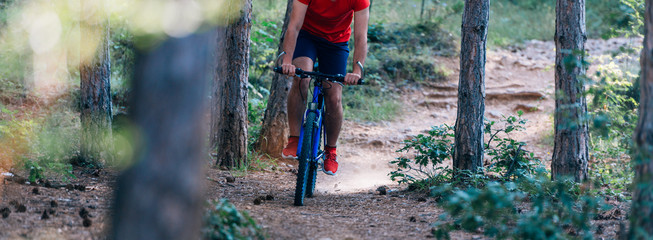 Fit cyclist riding his bike downhill through a forest ( woods ) while wearing a red shirt and red...