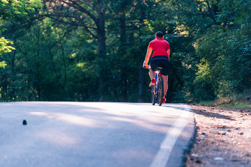 Fototapeta premium Tall handsome biker rides his bicycle on sunset in a lovely magical forest.