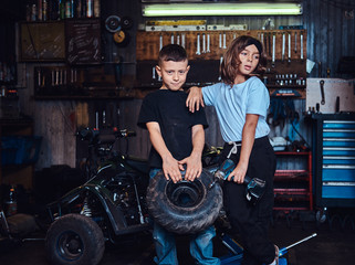 Obraz na płótnie Canvas Pretty little kids are holding weel and screwdriver while posing for photographer at auto service.