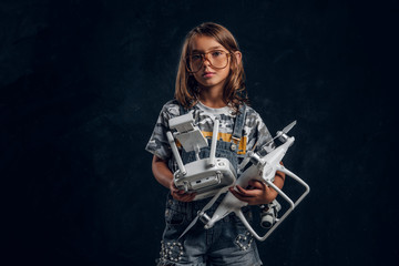 Pretty girl in glasses is posing for photographer at dark studio while holding controller and drone.