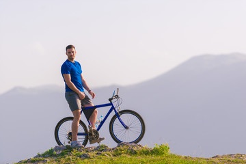 Fototapeta premium Fit mountain biker riding his bike through green grass on top of a mountain.