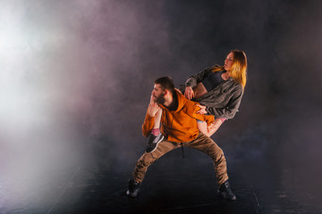 Strong male dancer and an elegant female dancer perform an exotic and unique dance moves in front of a black background while wearing urban clothes.