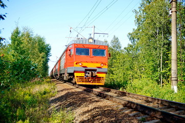 Obraz premium The electric train moves on rails. Around the forest. Sunny day.