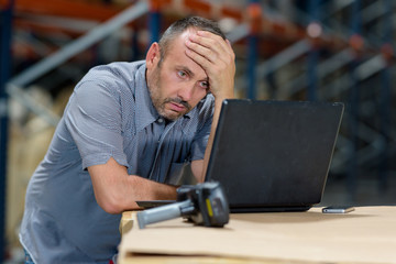 worried businessman working on computer in a warehouse - obrazy, fototapety, plakaty