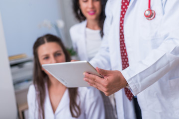 Defocused view of two nurses ( female physicians ) and a male doctor looking in a tablet at the...