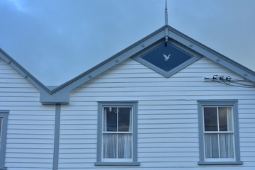 Facade detail of vintage wooden house with rectangular windows and one diamond-shaped window under roof arch.