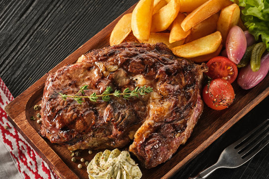 Ribeye steak with potatoes, onions and baked cherry tomatoes. Juicy steak with flavored butter