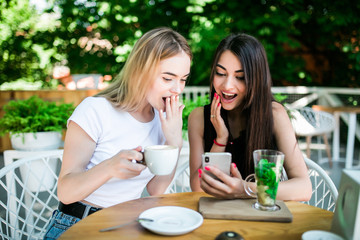 Two young attractive women drinking coffee at a restaurant and looking at phone