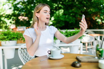 Young woman talking video call on the phone in a restaurant or cafe. Afternoon coffee breaks and...
