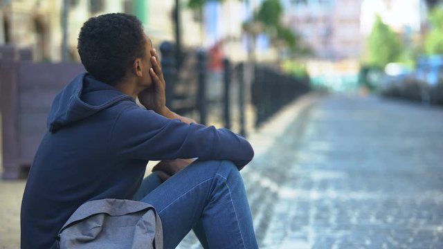 Sad mixed-race teenager sitting on sidewalk, relationship problems, awkward age