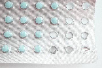 Foil packet of little round pills on white background. Close-up blue medicine tablets packed in blister. Macro drugs in using