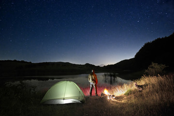 Man And Wild Camp By The Lake Under Starry Sky